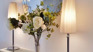 Una consola blanca con un espejo, dos lámparas y un florero con flores.