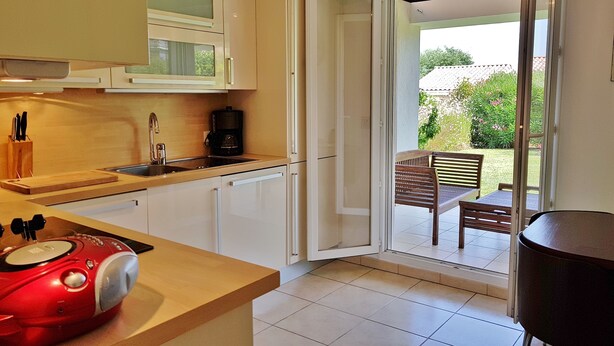 Una cocina con armarios blancos, un electrodoméstico rojo y un ventanal corredero que da a un patio exterior con una mesa y sillas de madera.