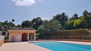 Una piscina con un pequeño pabellón, rodeada por una valla y árboles.