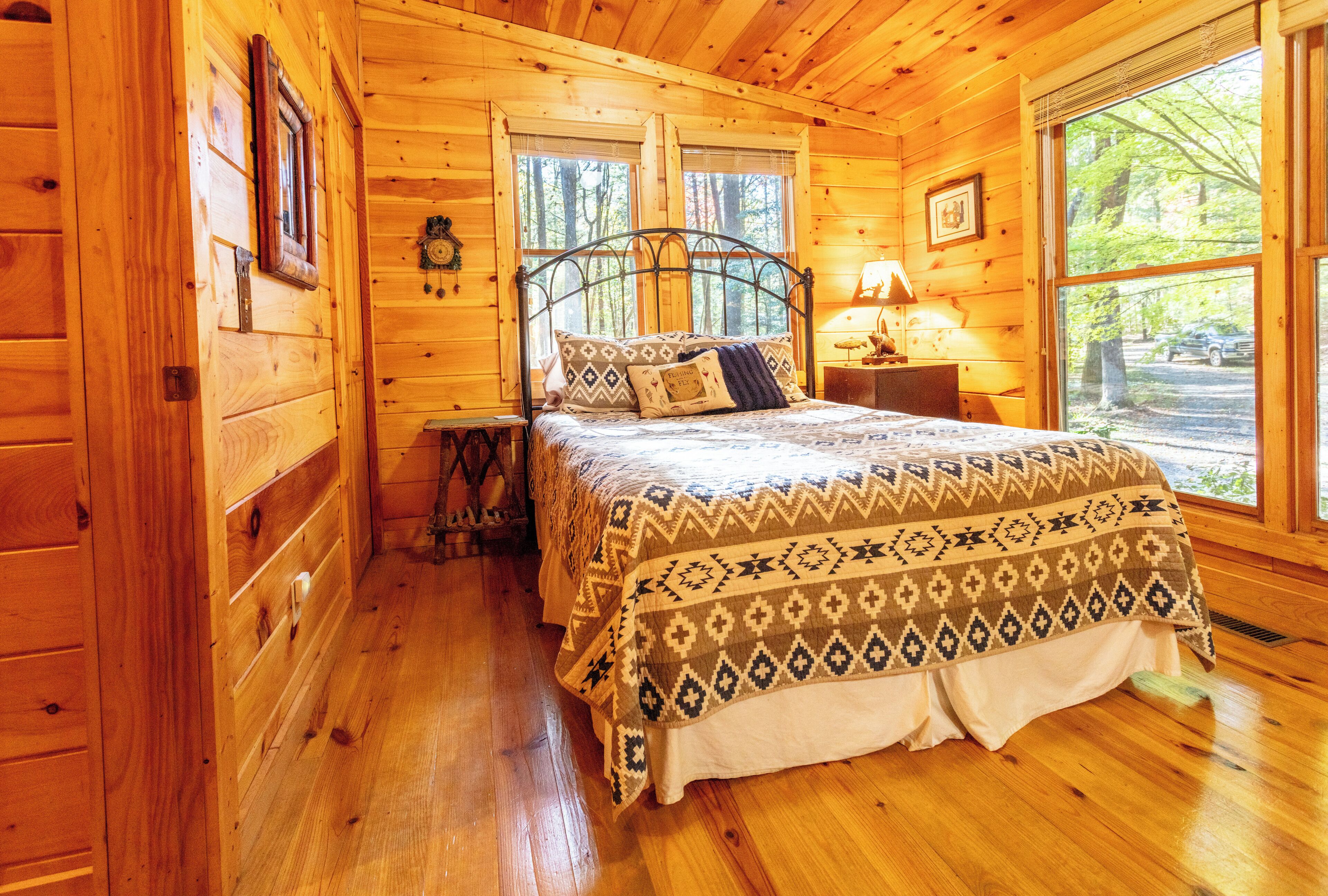 Een slaapkamer in een houten chalet met een bed, nachtkastje en raam.