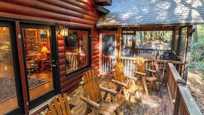 A log cabin with a deck, wooden chairs, and a visible interior with a fireplace. - Rushing Creek Cabin, Private Haven, 5 Acres to Explore (Ellijay)