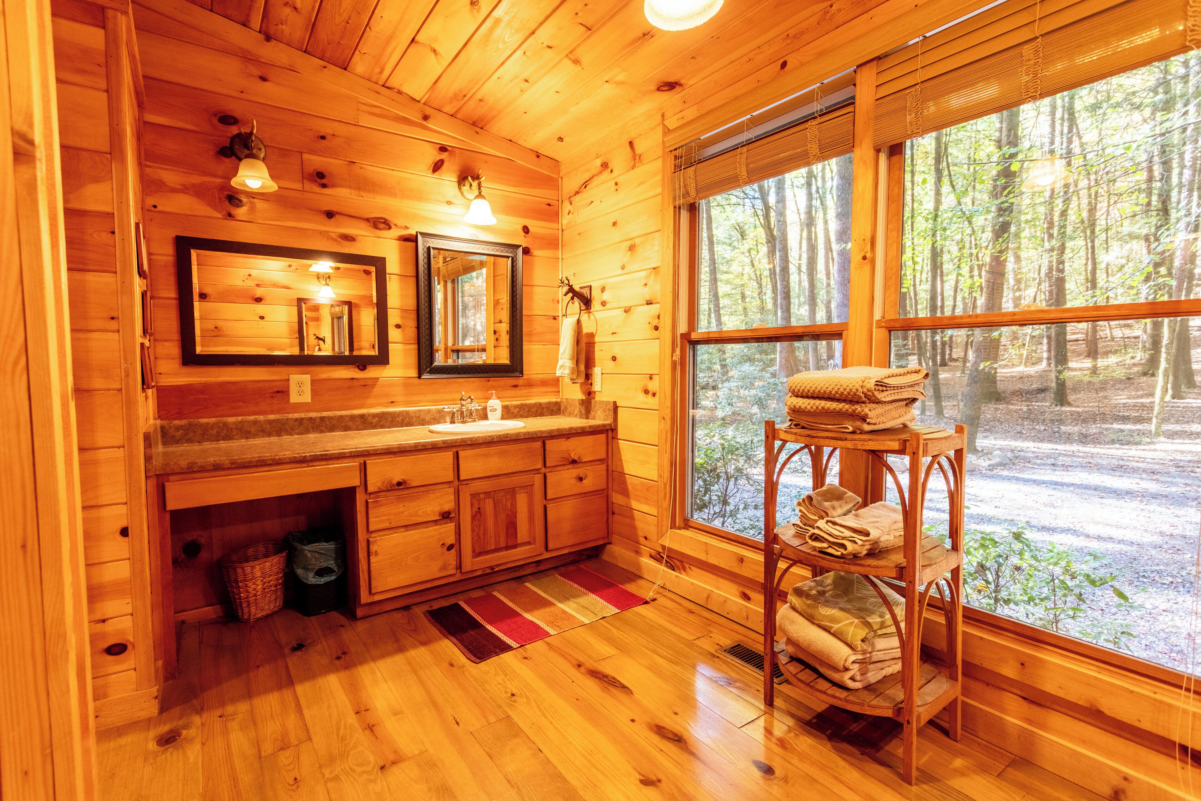 A wooden cabin bathroom with a large window, wooden cabinets, a sink, and a towel rack.
