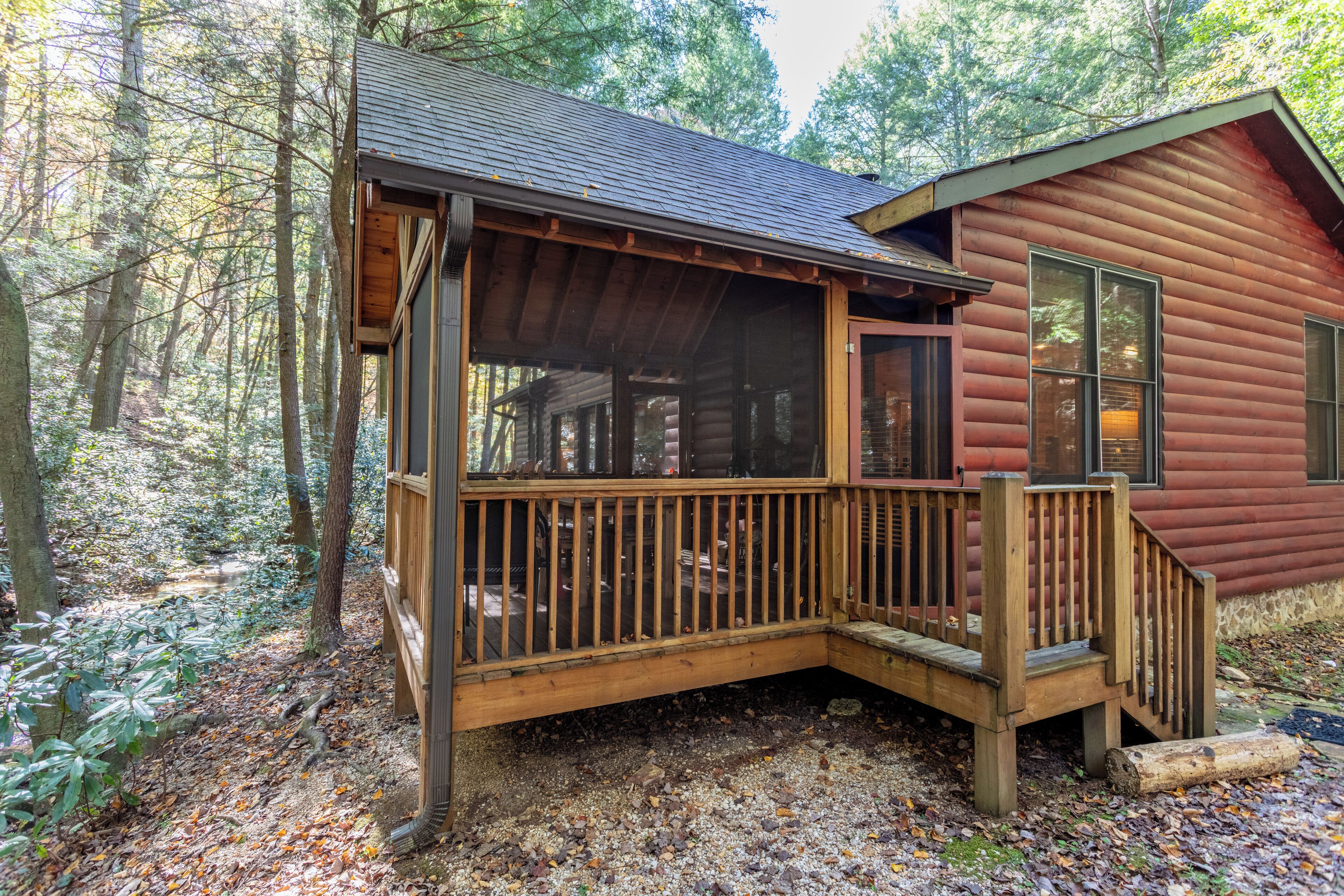 A cabin with a wooden deck and a porch, surrounded by a forest.