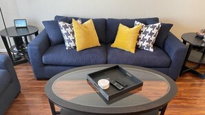 A modern living room with a blue sofa, two yellow pillows, a glass coffee table with a tray, and a small table with a clock. - 2 BD Townhome Old Town Scottsdale (Scottsdale)