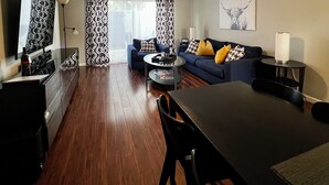 A modern living room with a dark wood floor, a blue sofa with patterned cushions, a dining table, and a ceiling fan. - 2 BD Townhome Old Town Scottsdale (Scottsdale)