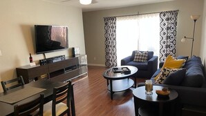 A modern living room with a flat-screen TV, a dining area with a wooden table and chairs, a sofa with patterned cushions, and a large window with patterned curtains. - 2 BD Townhome Old Town Scottsdale (Scottsdale)