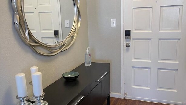 A hallway with a dark wooden floor, a black console table with two white candles and a glass bowl, a large mirror, and a white door with a handle. - 2 BD Townhome Old Town Scottsdale (Scottsdale)
