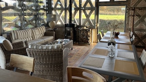 Una habitación acogedora con muebles de mimbre, una mesa con individuales, una chimenea y ventanas amplias con vistas al exterior.