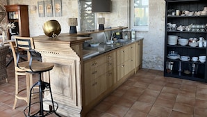 Una cocina con una barra de madera, un lavabo y una estantería con vajilla.