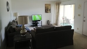 A living room with a sofa, a TV, a lamp, and a window with curtains. - 2 Bedroom condo in lovely quiet Naples location close to beach and shops (Naples)