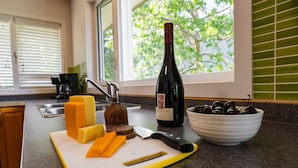 A kitchen counter with a cutting board, cheese, a bottle of wine, a bowl of olives, and a knife. - Eagle View, Paradise! 2 Beds, Hot Tub, Beach (Nelson)