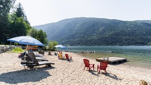 A beach with lounge chairs and umbrellas, a dock extending into the water, and a forested mountain in the background. - Eagle View, Paradise! 2 Beds, Hot Tub, Beach (Nelson)