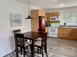A modern kitchen with wooden cabinets, a red refrigerator, a white stove, and a dining table with chairs.