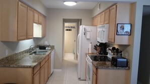 A kitchen with wooden cabinets, granite countertops, a refrigerator, a coffee maker, and a toaster. - 2/2 Condo, Ground Floor, 2 Parking Spaces, Pool (Saint Augustine Beach)