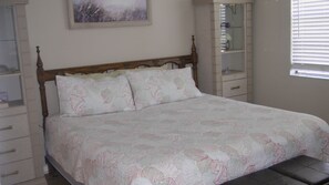 A bedroom with a wooden bed frame, a floral bedspread, and a nightstand with a lamp. - 2/2 Condo, Ground Floor, 2 Parking Spaces, Pool (Saint Augustine Beach)