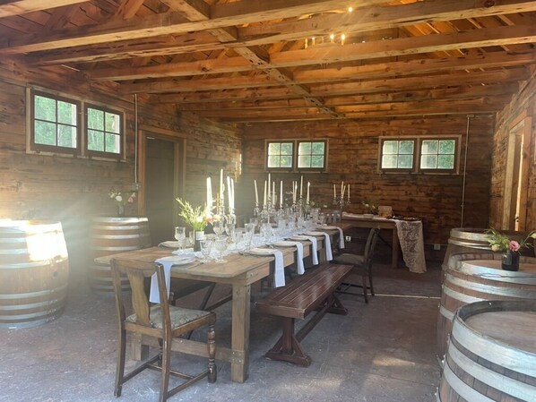 Un comedor rústico de madera con una mesa larga dispuesta para una comida, rodeado de barriles.