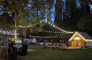 Evento al aire libre con luces colgantes, un escenario y un edificio pequeño.