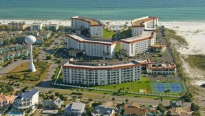 Ein Hotelkomplex an der Küste mit mehreren Gebäuden, einem großen weißen Turm und einem Strand im Hintergrund.
