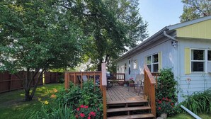 A wooden deck with a staircase leading to a house with a yellow exterior and white shutters. - Peaceful Cozy Home In A Rural Garden Farm Setting ~ "Bobolink" House (Carrington)