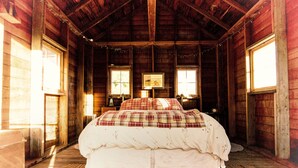 A cozy wooden cabin bedroom with a large bed, two windows, and a framed picture on the wall. - Peaceful Cozy Home In A Rural Garden Farm Setting ~ "Bobolink" House (Carrington)