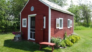 A red wooden cabin with a door open, a small bench, and potted plants. - Peaceful Cozy Home In A Rural Garden Farm Setting ~ "Bobolink" House (Carrington)