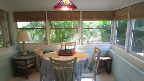 A dining area with a round table, four chairs, a small table with a lamp, and a window with blinds.