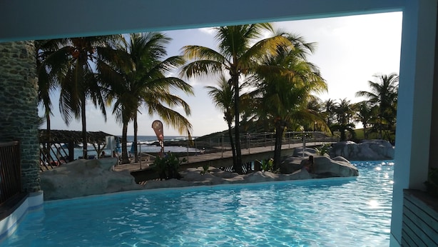 A pool area with clear water, palm trees, and a view of the ocean. - Marco Polo (Saint-François)