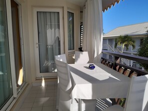 A balcony with a table and chairs, a sliding glass door, and a view of a building with a white facade and balconies. - Marco Polo (Saint-François)
