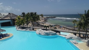 A resort pool with a view of the ocean, palm trees, and a beach area. - Marco Polo (Saint-François)