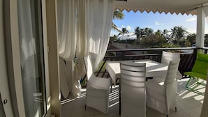 A balcony with a table and chairs, white curtains, and a view of palm trees and buildings. - Marco Polo (Saint-François)
