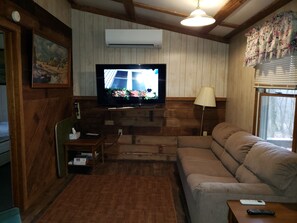 Een gezellige woonkamer met een televisie, houten wanden, een bank en een lamp.