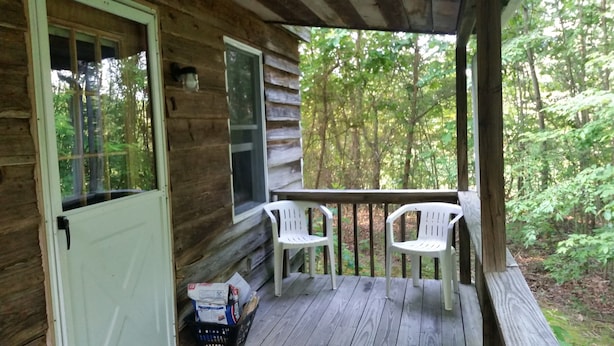 A wooden cabin with a porch, two white plastic chairs, and a basket with items on the floor.