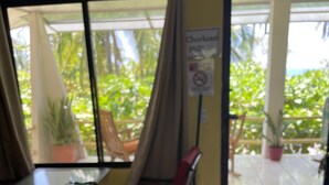 Quarto com uma mesa, uma cadeira de balanço e vista para o exterior através de uma porta de vidro.
