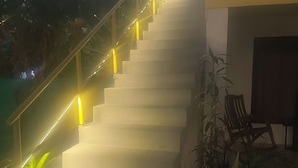 Escada com corrimão e luzes amarelas, levando a uma entrada de edifício.