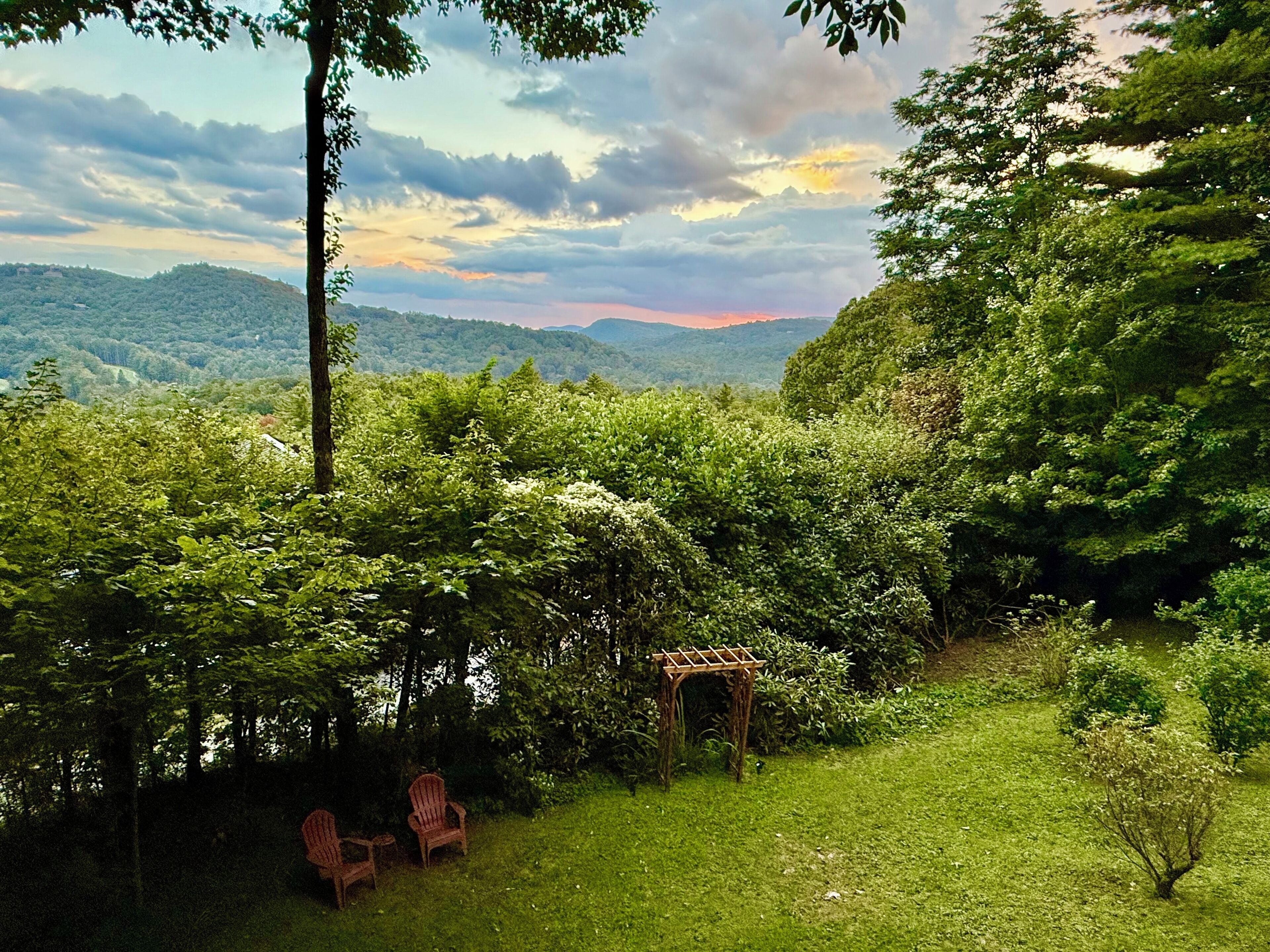 A lush garden with a wooden pergola and two Adirondack chairs.