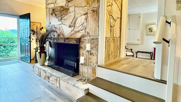 Un salon moderne avec une cheminée en pierre, un plancher en bois et un escalier menant à un niveau supérieur.