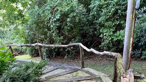 Un chemin de pierres qui traverse un jardin agrémenté de rampes en bois et d’un poteau en bois rustique.
