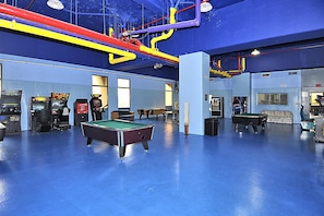 Espaço de lazer com mesas de bilhar, jogos de arcade e uma estrutura de teto colorida.