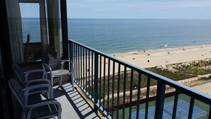 Un balcon avec des chaises donnant sur une plage et un court de tennis.