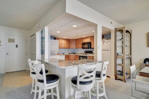 Une cuisine moderne avec des meubles en bois, un îlot central doté de tabourets de bar et un micro-ondes encastré.