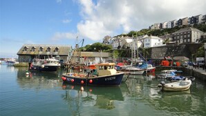 A harbor with boats docked, a building with a sloped roof, and houses along the shore. - Tinners Forge - One Bedroom Cottage, Sleeps 2 (Polgooth)