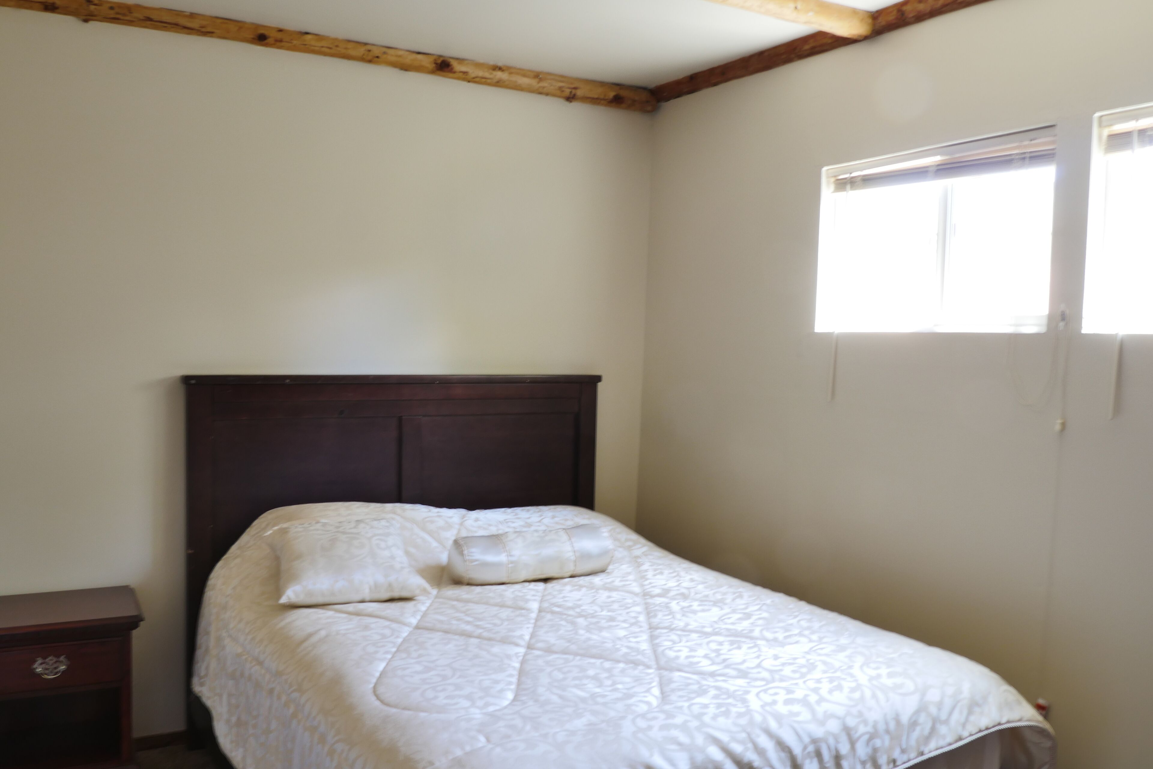 A bedroom with a wooden headboard, a bed with a quilt, a nightstand, and a window with blinds.