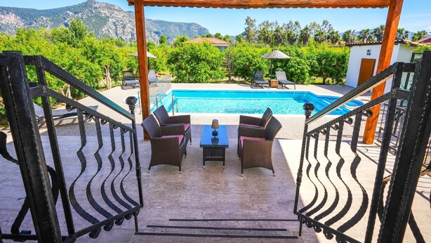 Uma área externa coberta com piscina, móveis de vime e vista para montanhas.