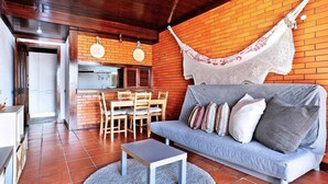 Un espacio de sala acogedor con pared de ladrillo, una hamaca, una mesa de comedor con sillas y un sofá con cojines.