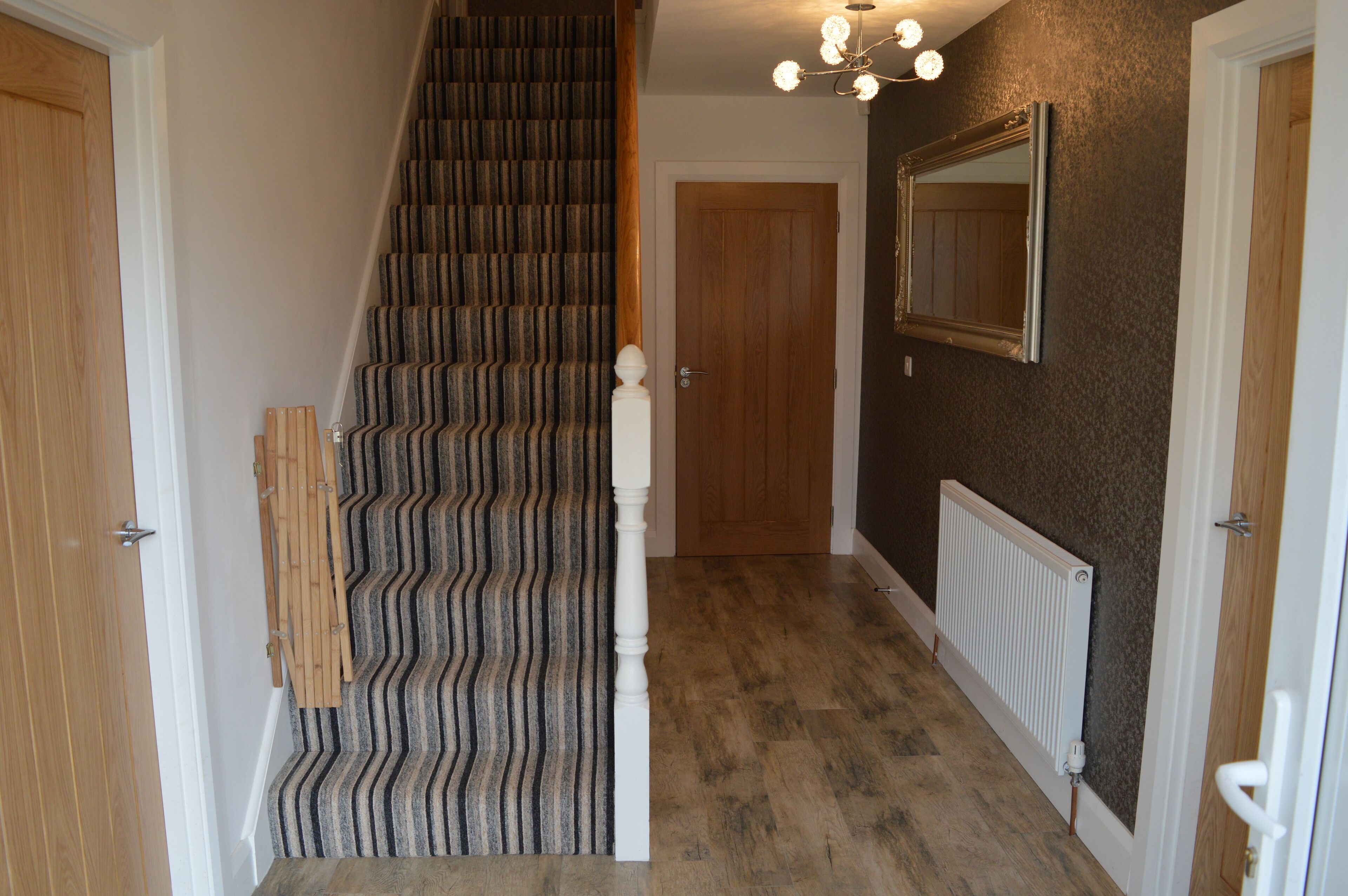 A staircase with a striped carpet, a wooden door, a white radiator, and a mirror on the wall.
