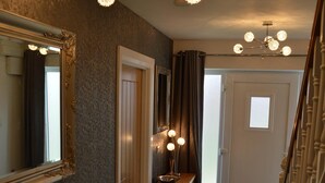 Een gang met een spiegel, een kroonluchter en een deur naar een andere kamer.