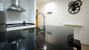 Eine moderne Küche mit Spüle aus Edelstahl, Dunstabzugshaube und am Wand montiertem Wasserhahn. An den Wänden befinden sich schwarze Dekorationen und ein weißes Regal.