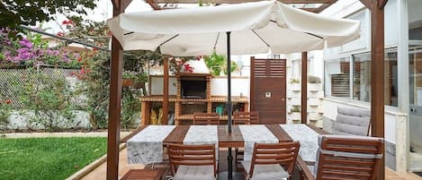An outdoor patio with a wooden pergola, a barbecue area, and a table with chairs.