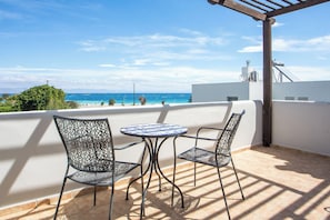 A balcony with a table and chairs, overlooking a coastal view.