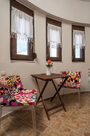 A room with two chairs, a table, and three windows with curtains.